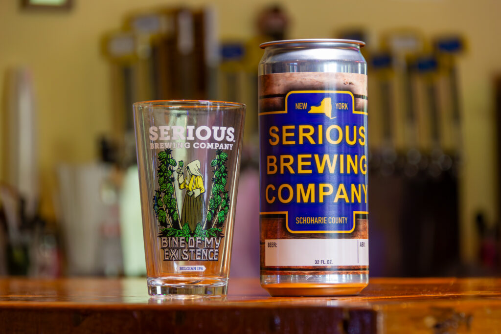 "Bine of My Existence IPA" beer in a can, next to a glass with artwork.