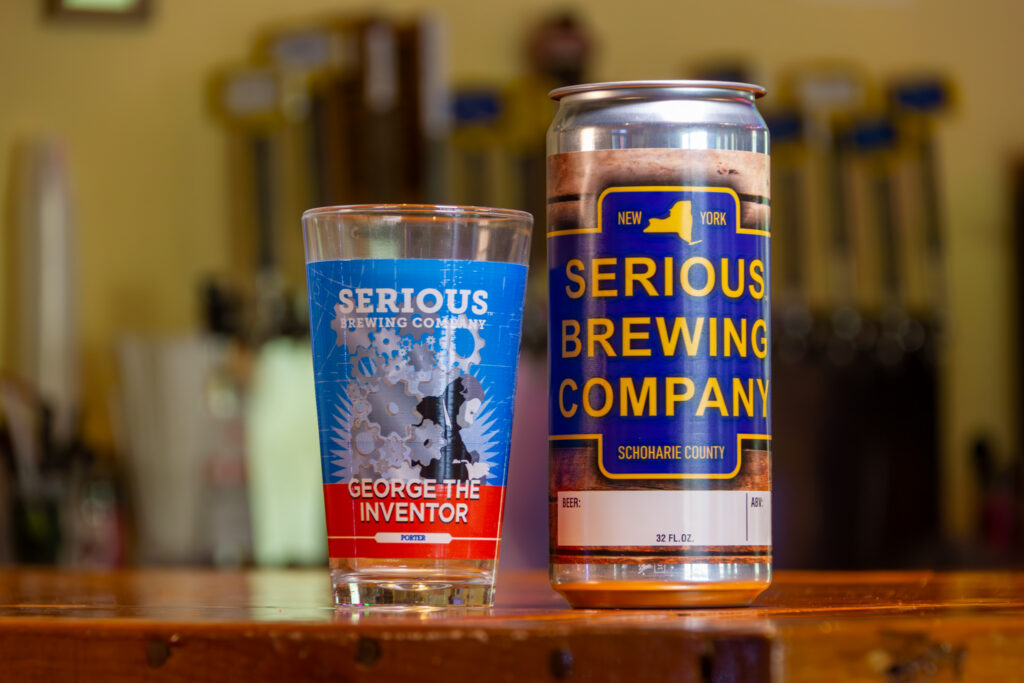 "George the Inventor Porter" beer in a can, next to a glass with artwork of gears on a blue background.