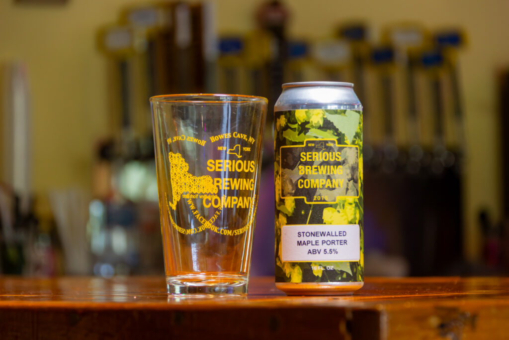 "Stonewalled Maple Porter" beer in a can, next to a glass with the Serious Brewing logo.